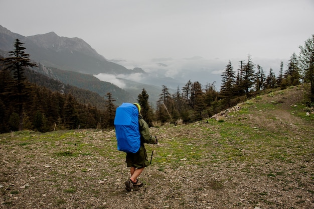 Girl in the raincoat walking with hiking backpack and sticks