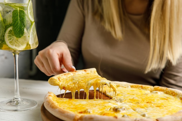 girl raises pizza over the table The cheese stretches