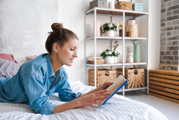 Girl reading book in bed lying on her stomach smiling happy and relaxed