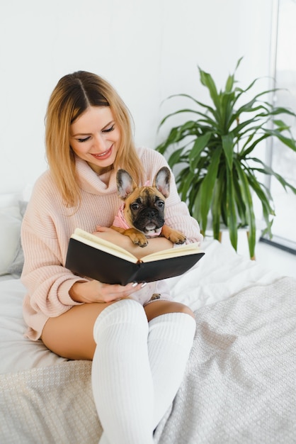 Girl reading a book. Cute girl reading a book with her dog at home. Pretty stylish girl.