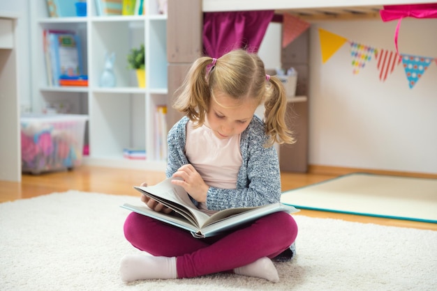 家のカーペットに座って本を読んでいる女の子