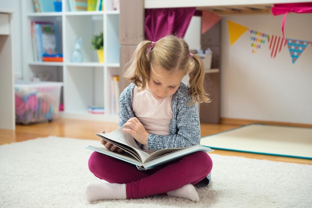 家のカーペットに座って本を読んでいる女の子