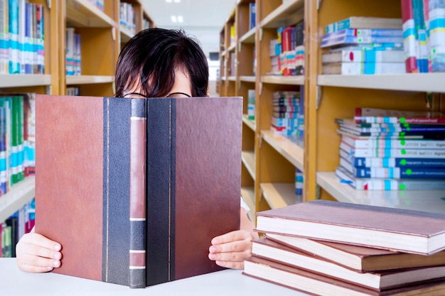 Foto ragazza che legge un libro seduta in biblioteca