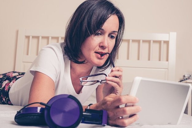 girl reading a news on a tablet with some glasses in her hand 