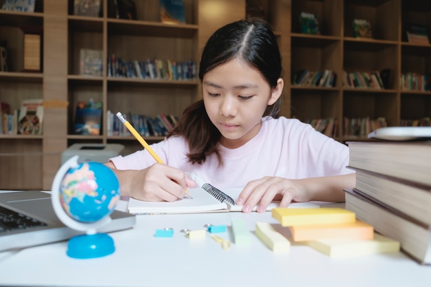 Girl reading and writing in library of school.