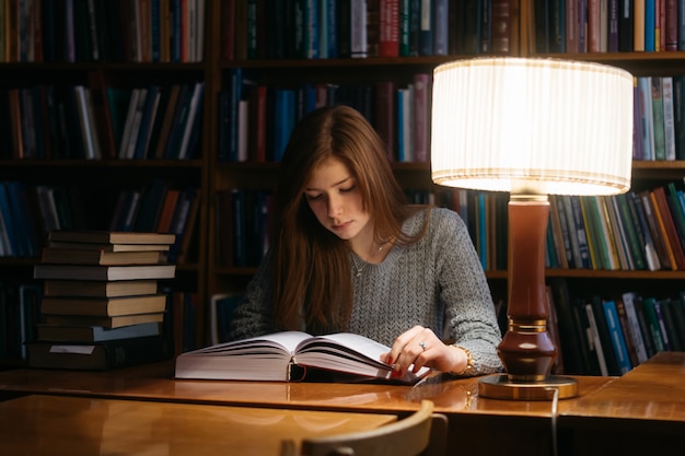 A girl reads a book in a library while sitting at a table. The girl in the library