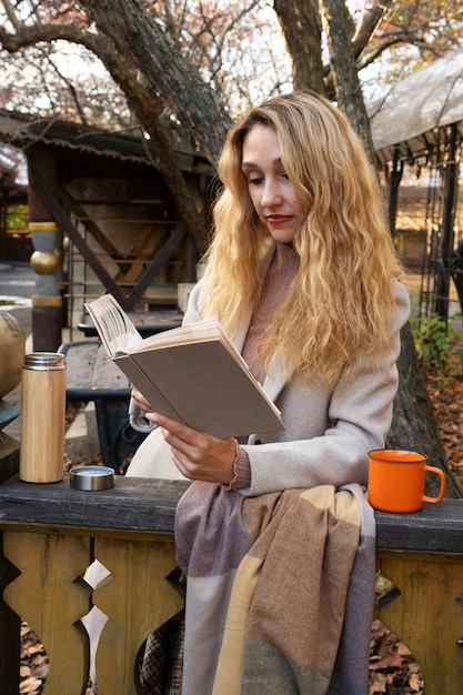 A girl reads a book on the terrace in the fall and drinks tea