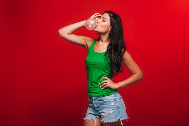 Girl on a red background blowing bubbles of gum