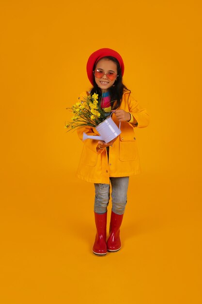 a girl in a red beret with pink glasses in a yellow raincoat holding a bucket with flowers