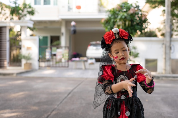 頭に赤い花を乗せた赤と黒のドレスを着た女の子が家の前に立っています。