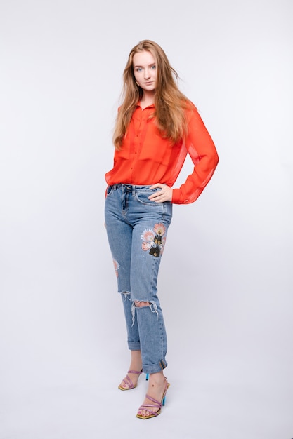 Girl in red blouse and jeans posing on isolated wall