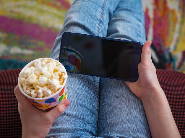 Girl on a red chair with a glass of popcorn in his hands