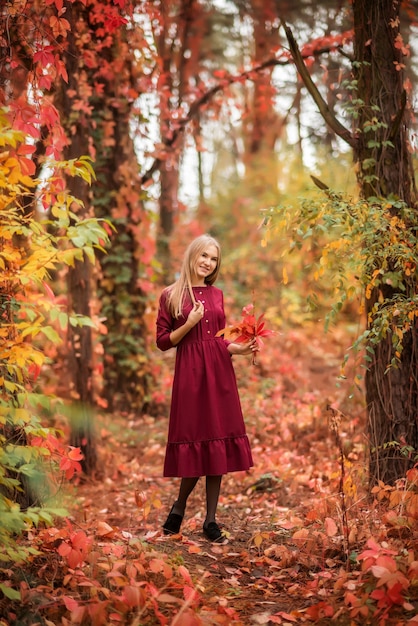 Girl in a red dress in the autumn forest. A beautiful fairy-tale forest. A bouquet of leaves in your hands