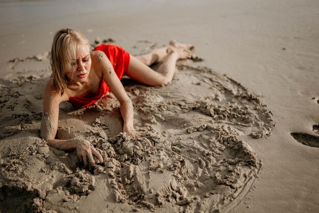 Photo a girl in a red dress lies on the white sea sand
