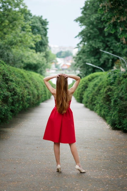 A girl in a red dress and long hair in a garden with green plants