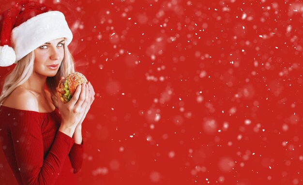 Girl in red dress and santa hat with burger in hands