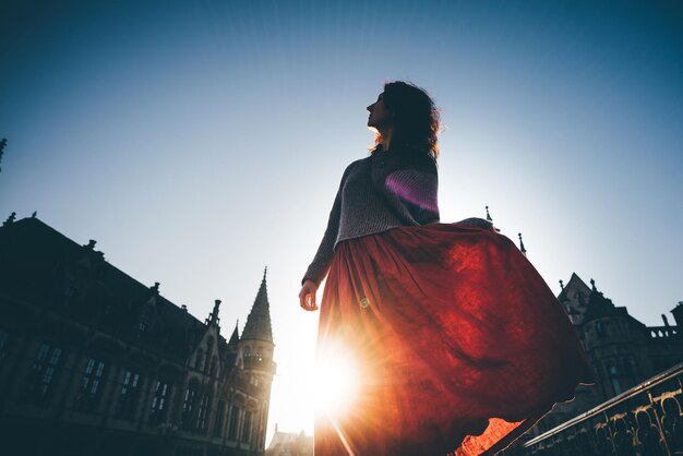 Girl in the red dress walking on the city centre at the sunrise, enjoying the sights alone. woman dansing in backlight. ghent, belgium