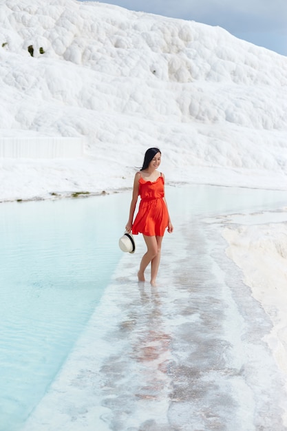 Girl in red dress on white travertines, water