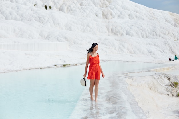 Girl in red dress on white travertines, water