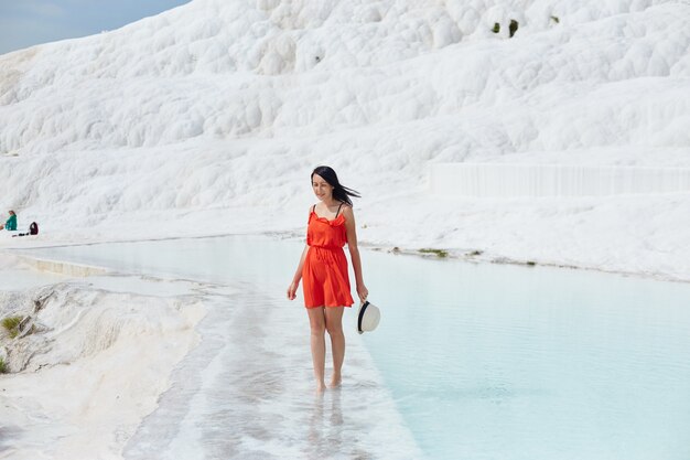 Girl in red dress on white travertines, water