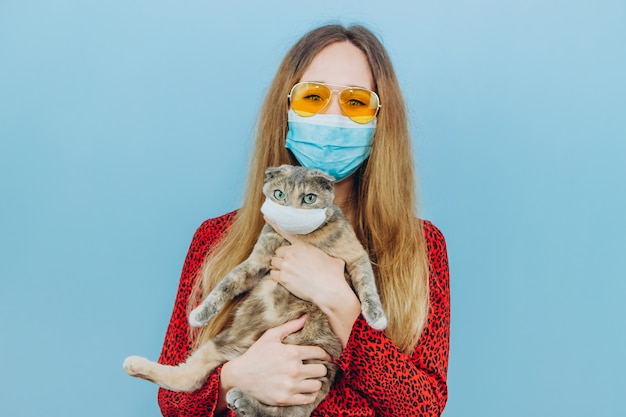 Girl in a red dress with a medical mask on her face holds a cat. 