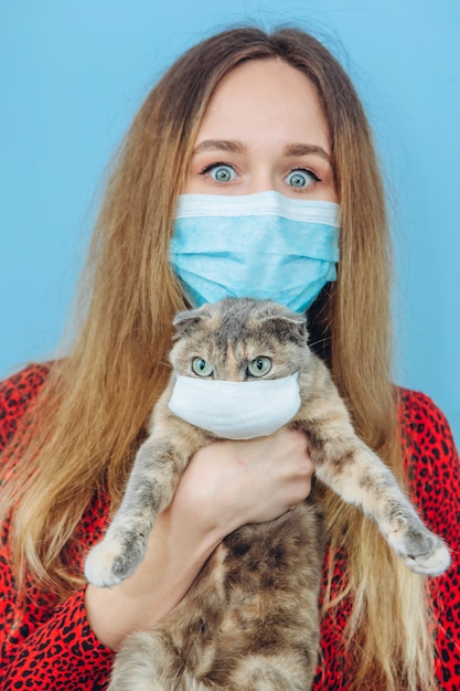 La ragazza in un vestito rosso con una mascherina medica sulla sua faccia tiene un gatto.