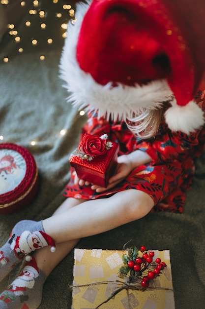 A girl in a red hat of santa claus sorts out gifts against the background of a Christmas tree