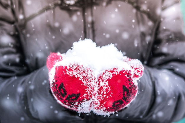 Ragazza in muffola rossa che tiene una manciata di neve