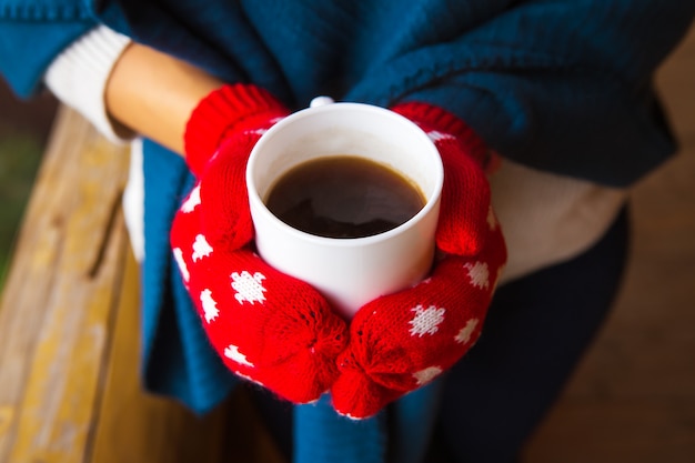 コーヒーのカップを保持している赤いミトンの女の子