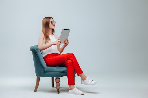 Girl in red pants sitting in a chair and using her tablet