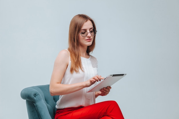 Girl in red pants sitting in a chair and using her tablet