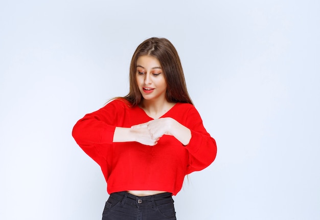 Ragazza in camicia rossa che indica il suo orologio.