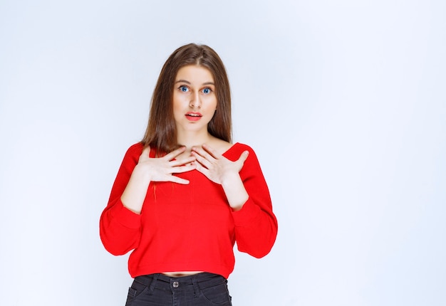 Girl in red shirt pointing at herself. 