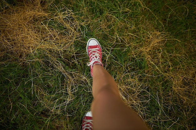 Girl in red sneakers walks on the grass top view