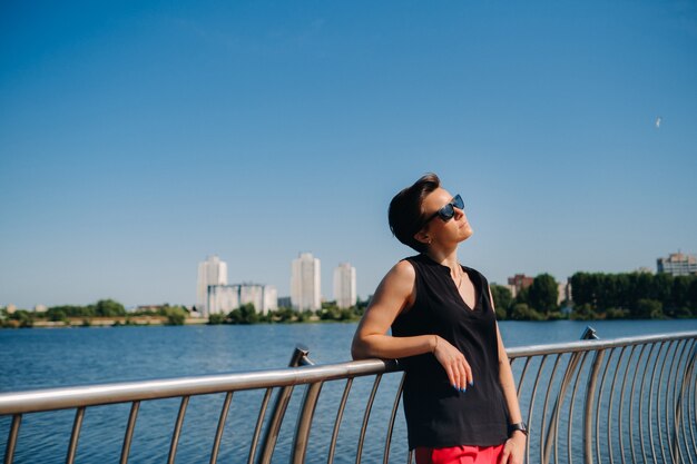 A girl in a red suit stands on a pier near the lake.