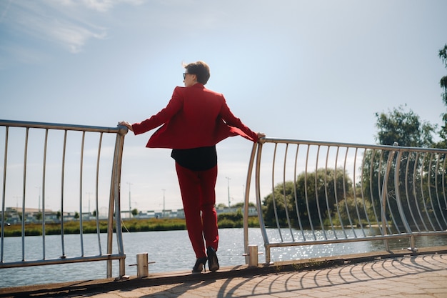 A girl in a red suit stands on a pier near the lake.