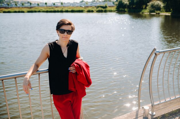 A girl in a red suit stands on a pier near the lake.