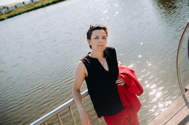 A girl in a red suit stands on a pier near the lake