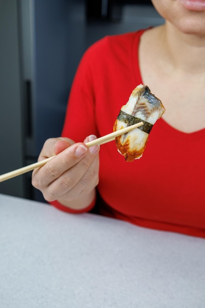 A girl in a red sweater holds sushi with conger eels with chopsticks Seafood