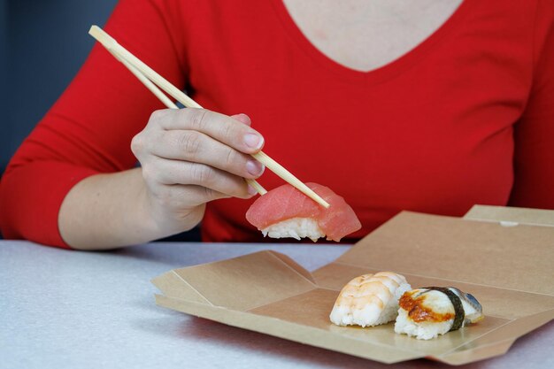 A girl in a red sweater holds tuna sushi with chopsticks Seafood