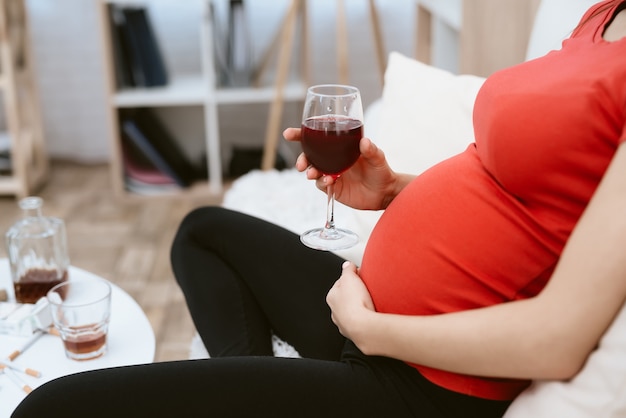 Девушка в красной футболке беременна пьет вино.