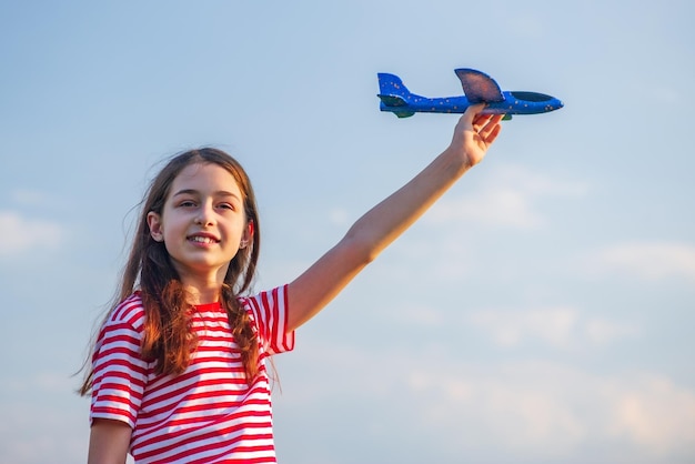 Girl in a red Tshirt with a white stripe A teenage girl with a blue toy airplane in her hands against the sky