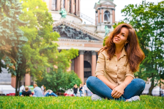 A girl relaxes on the grass in the center of St. Petersburg in front of St. Isaac's Cathedral