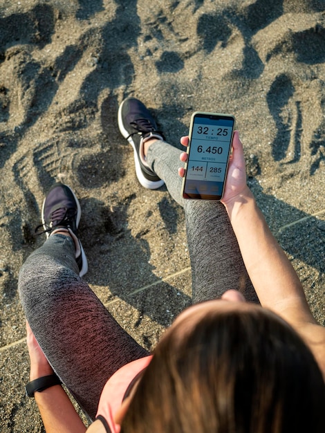 Girl resting after running while watching running app on mobile phone