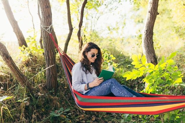 Девушка отдыхает в парке с книгой в гамаке