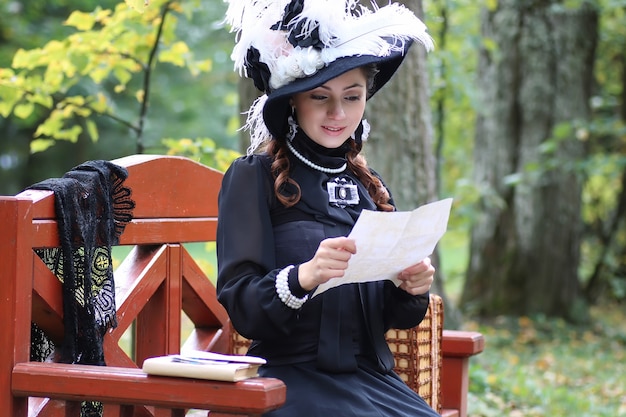 지난 세기에 복고풍 드레스를 입은 소녀가 벤치에서 편지를 읽었습니다.