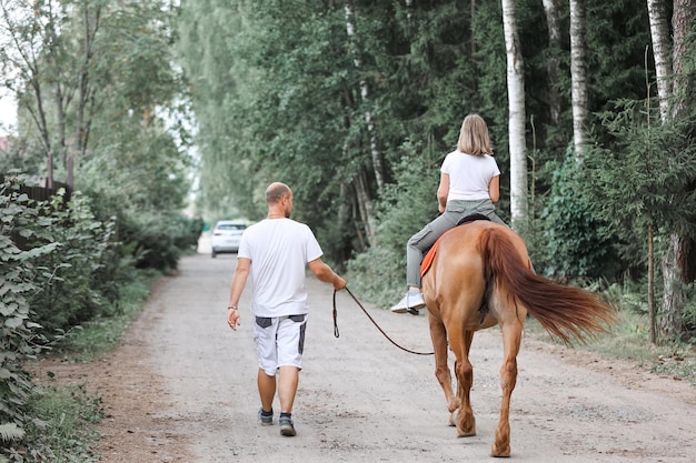 A girl rides a horse accompanied by her father in the hot summer