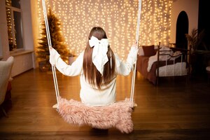 Photo a girl rides a swing with a bow in her hair in the background is a christmas tree