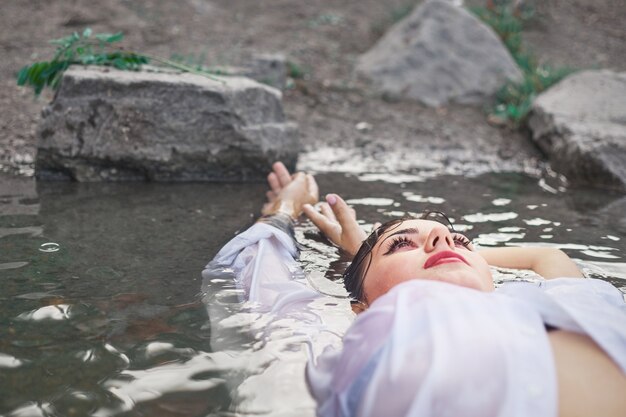 Photo girl in the river on a stone in a white shirt, one