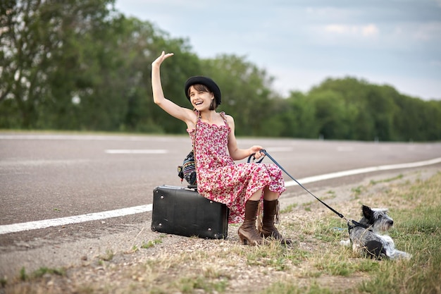 古いスーツケースと犬と一緒に道路上の女の子が自動車を止めた